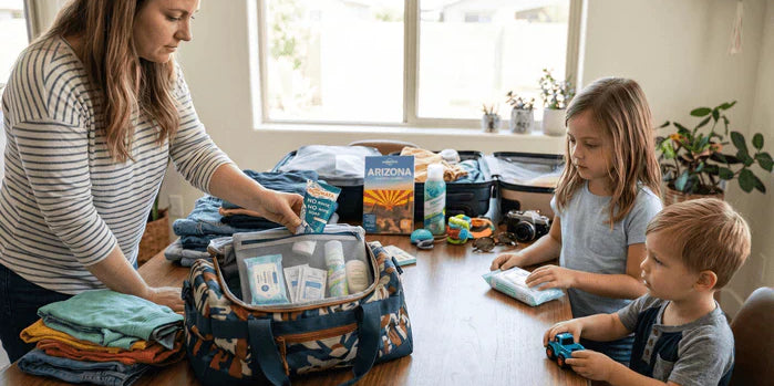 An image of a parent packing NOWATA rinse-free soap into a family travel bag with kids nearby, illustrating a no-water hygiene kit for keeping children healthy on vacation.