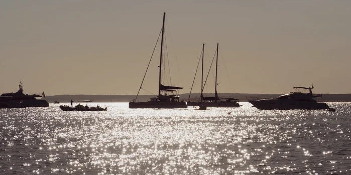 An image of a sailboat and a small fishing boat on open water.
