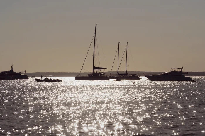 An image of a sailboat and a small fishing boat on open water.