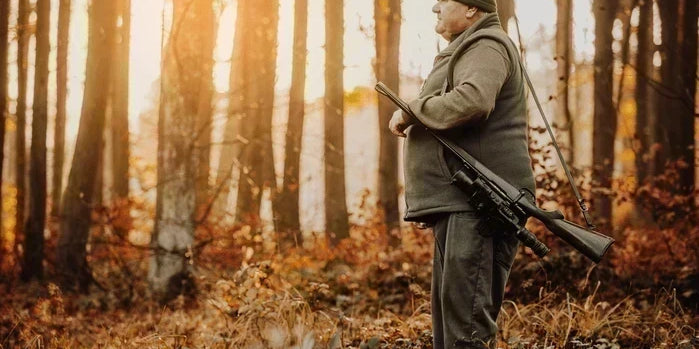 An image of a hunter in blaze orange walking through autumn woods.