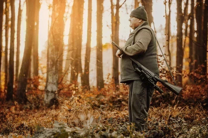 An image of a hunter in blaze orange walking through autumn woods.