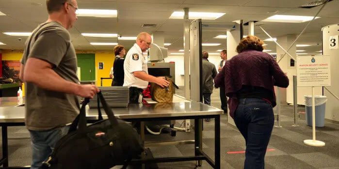An image of travelers at an airport TSA security checkpoint with carry-on bags.
