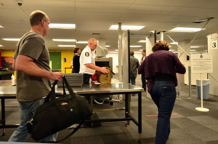 An image of travelers at an airport TSA security checkpoint with carry-on bags.