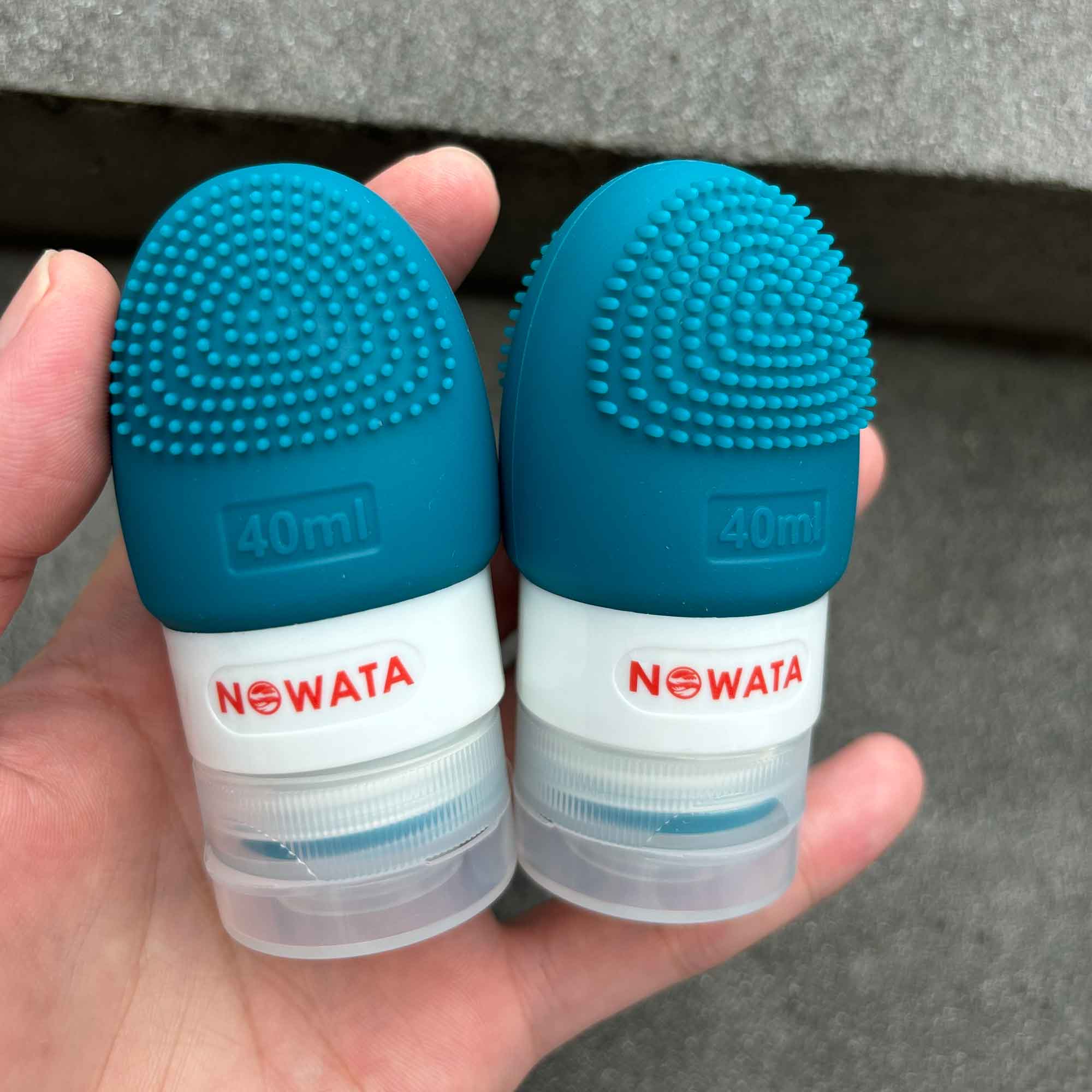 Two refillable silicone bottles with integrated silicone brush in hand